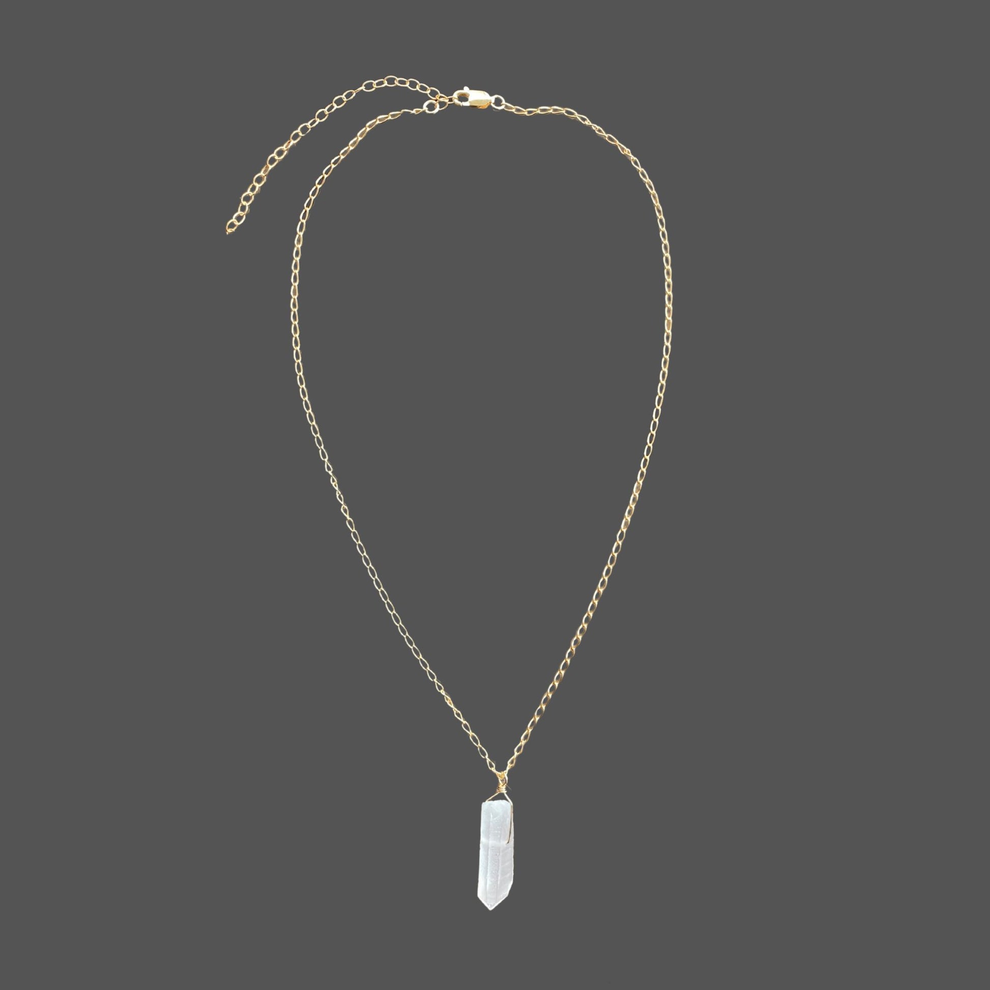 Gemstone pendant necklace with raw  clear quartz point pendant on a delicate gold chain. Shown alone on plain background.