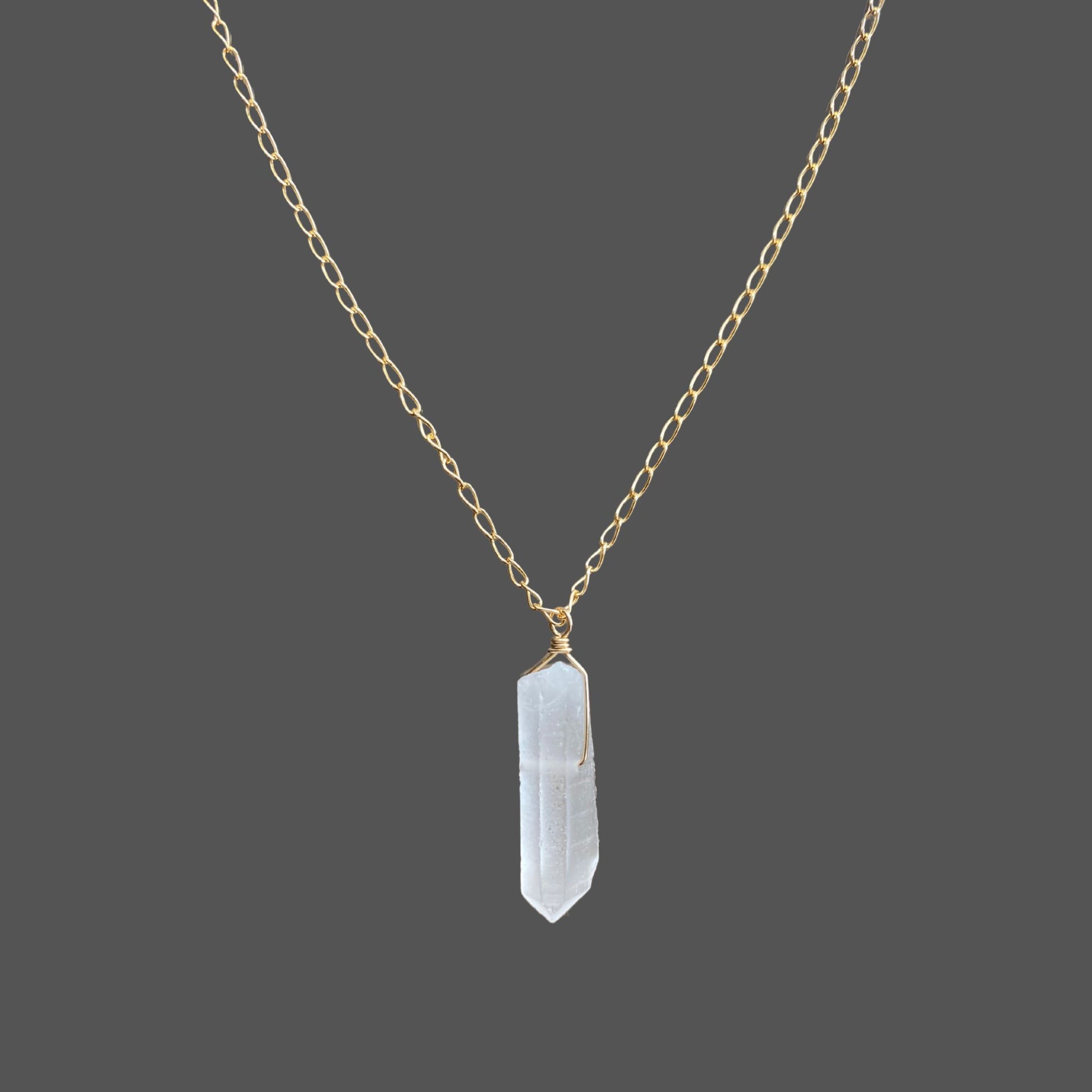 Close-up view of raw clear quartz point pendant on gemstone necklace with gold chain.