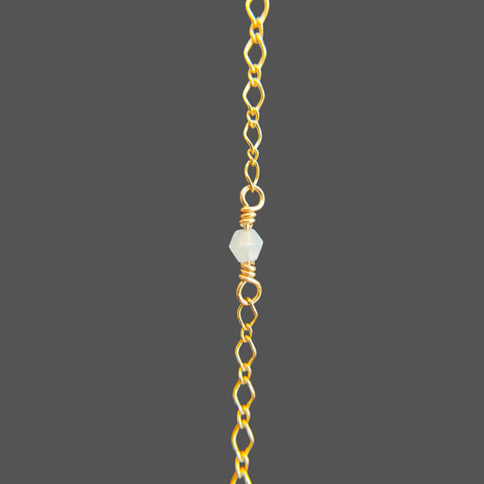 Close-up of a wire-wrapped aquamarine gemstone at the center of a gold chain bracelet.