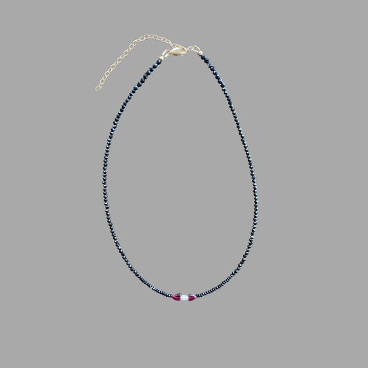 Beaded gemstone necklace, with black tourmaline and one rice pearl at the center with a garnet gem on each side of the pearl.