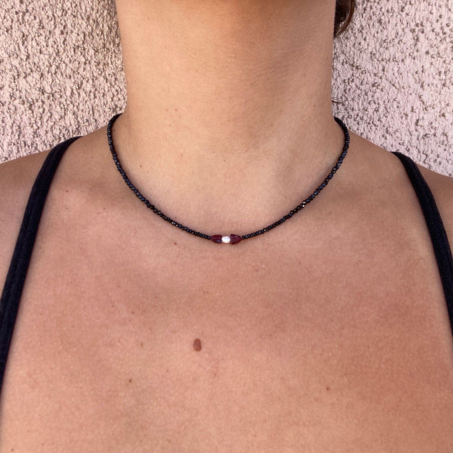 Gemstone necklace shown on model, with black tourmaline beads and one rice pearl at the center flanked by a garnet on each side.