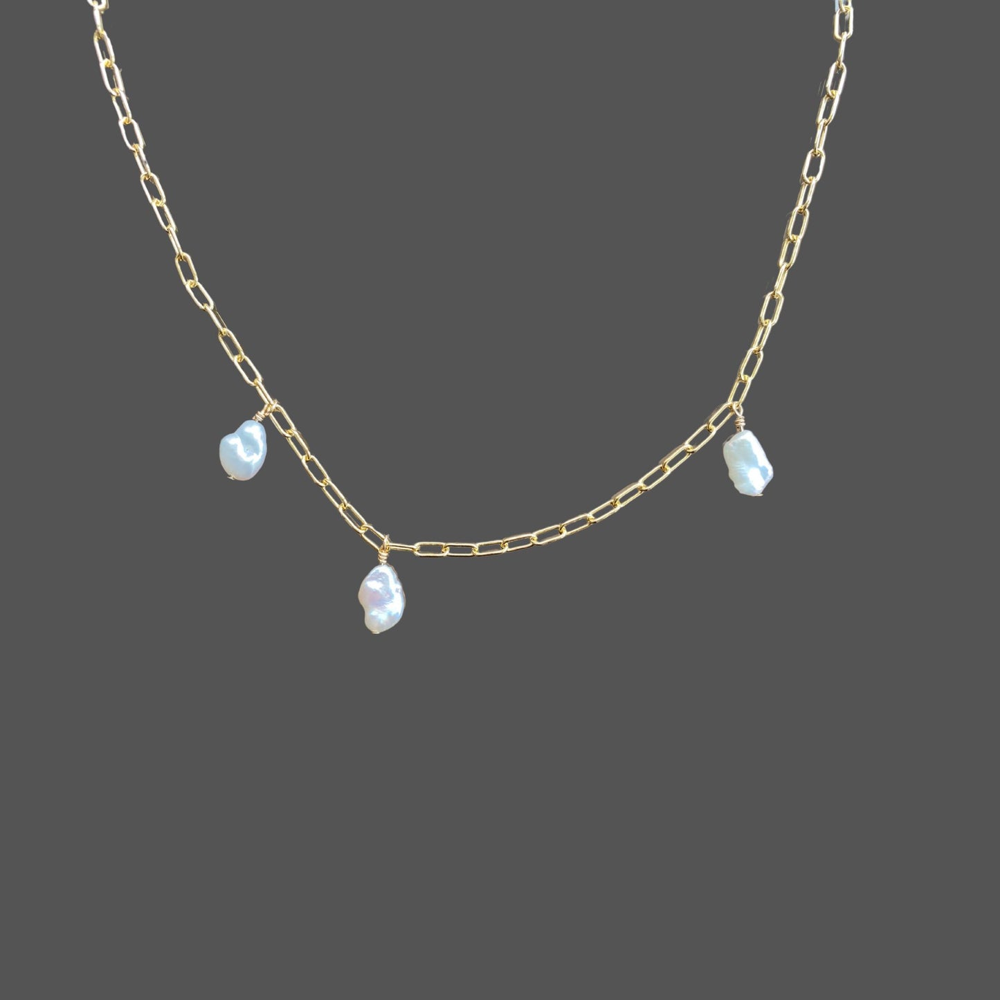 Close up of pearls on gold paperclip chain necklace, with 3 asymmetrically placed baroque pearls.