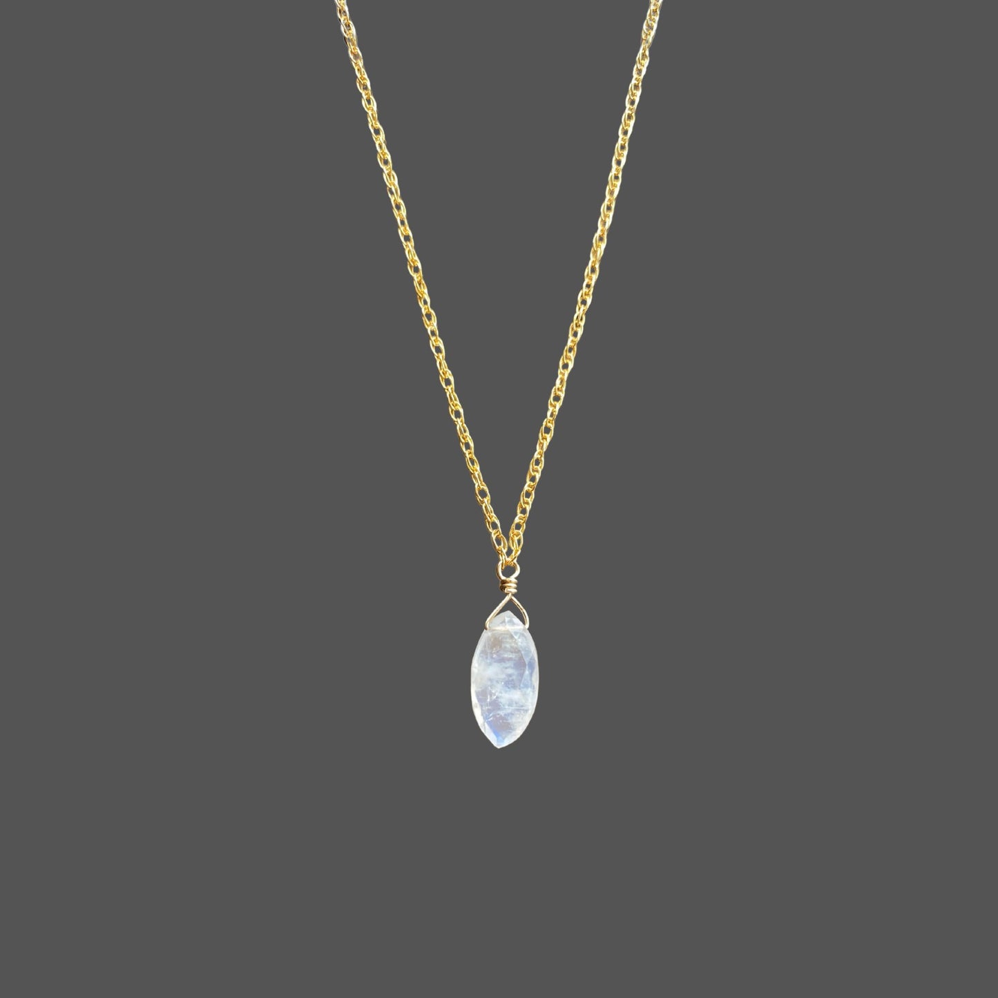 Close-up view of marquise shaped rainbow moonstone pendant on gemstone necklace with gold chain. Shown alone on plain background.
