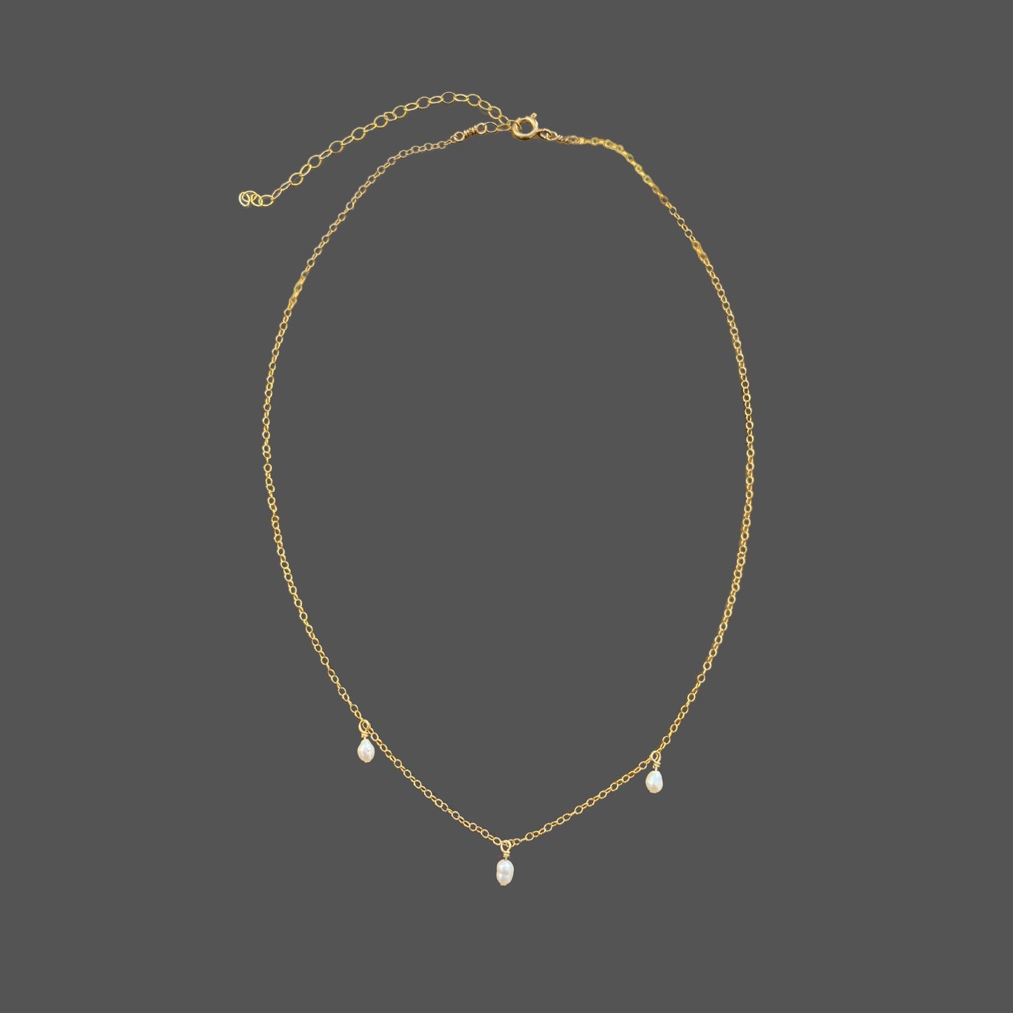 Pearl necklace with delicate gold chain and three equally spaced rice pearls dangling from the chain at its center. Shown alone on plain background.