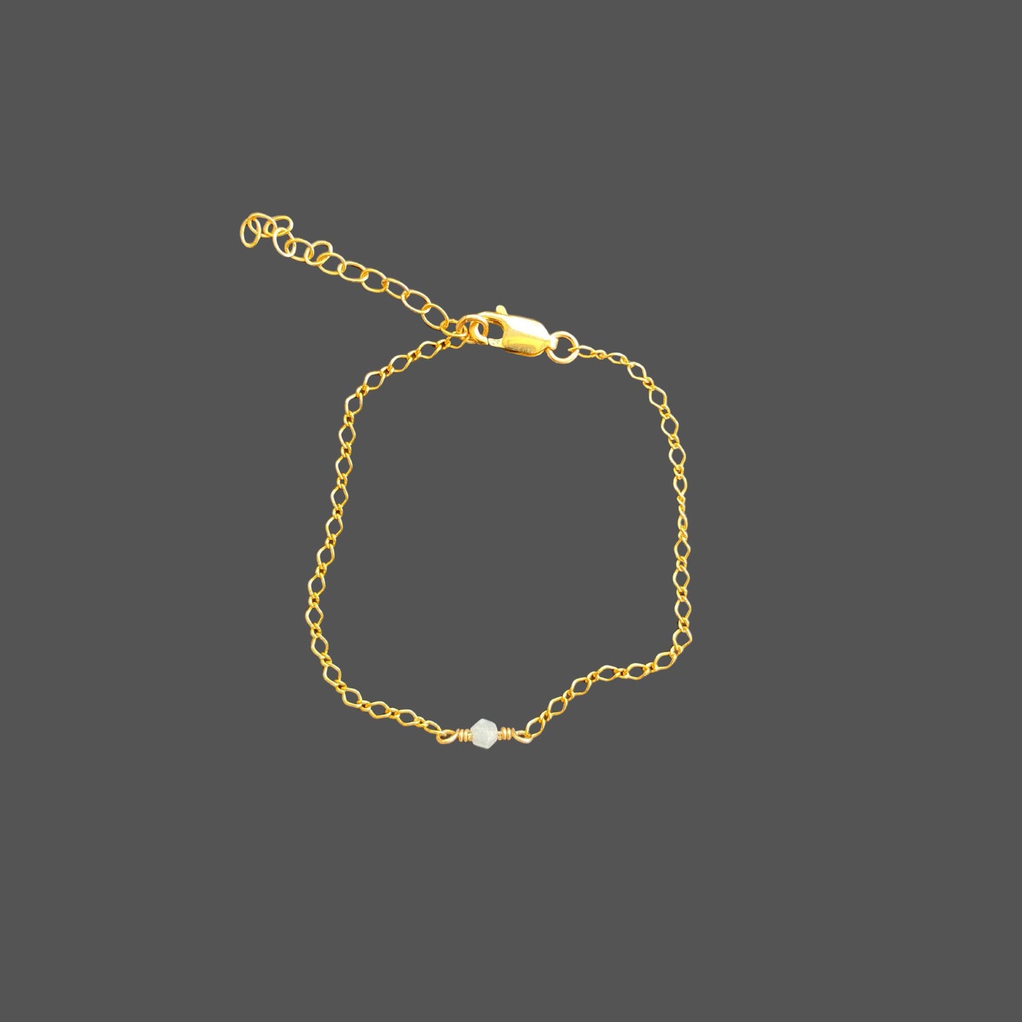 Dainty gold chain bracelet with a single aquamarine bicone gem centered on the chain.