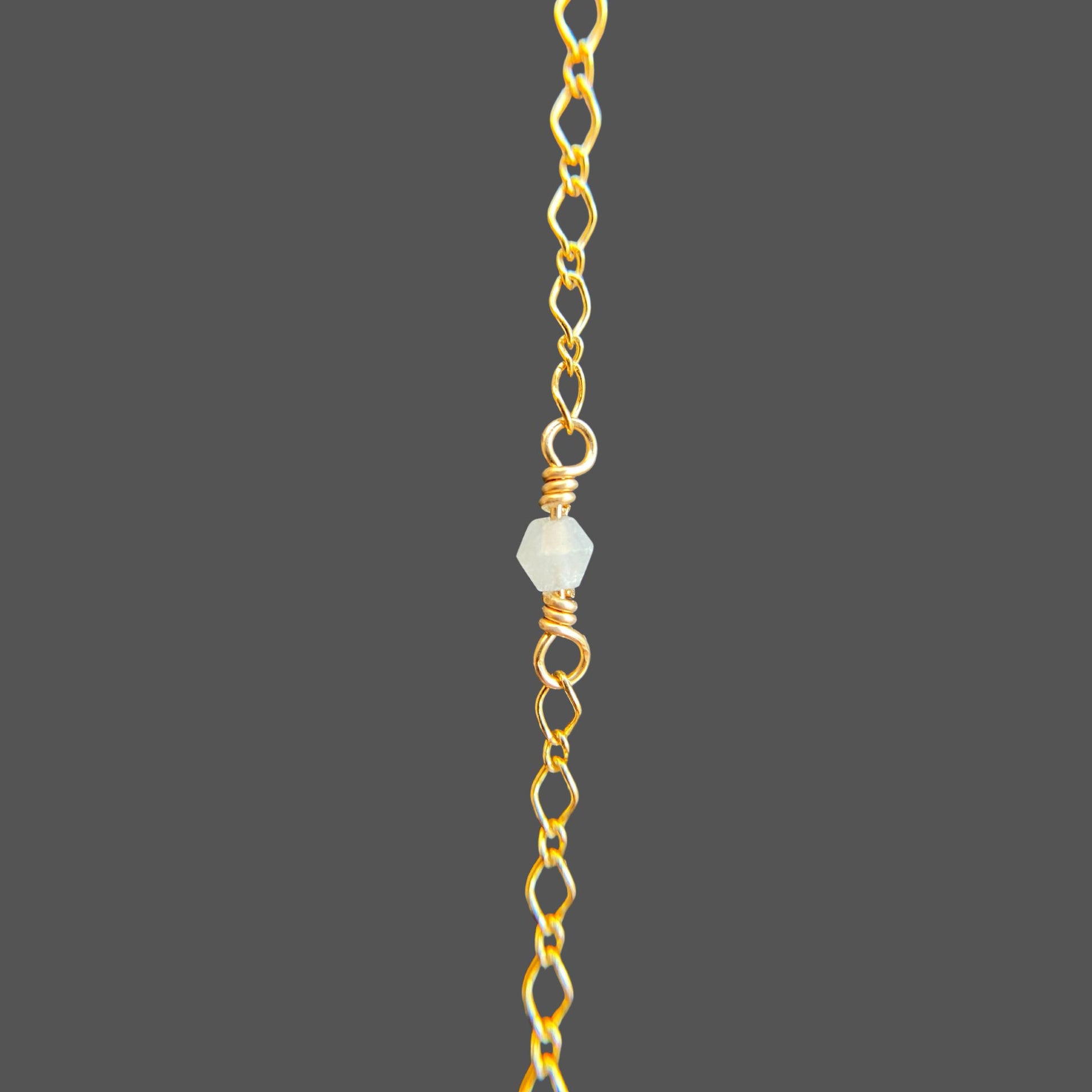 Close-up of a wire-wrapped aquamarine gemstone at the center of a gold chain bracelet.