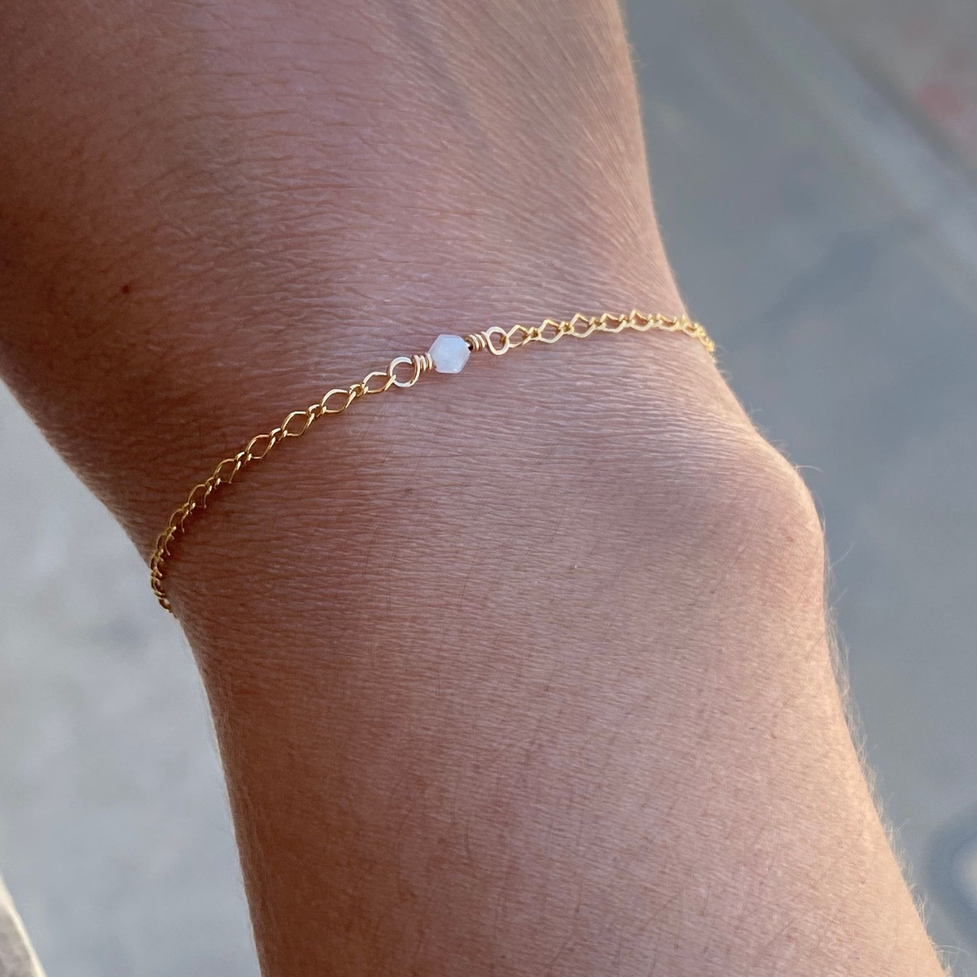 Dainty gold chain bracelet with an aquamarine gemstone centered on the chain, shown on a model. Only the model's wrist is visible.