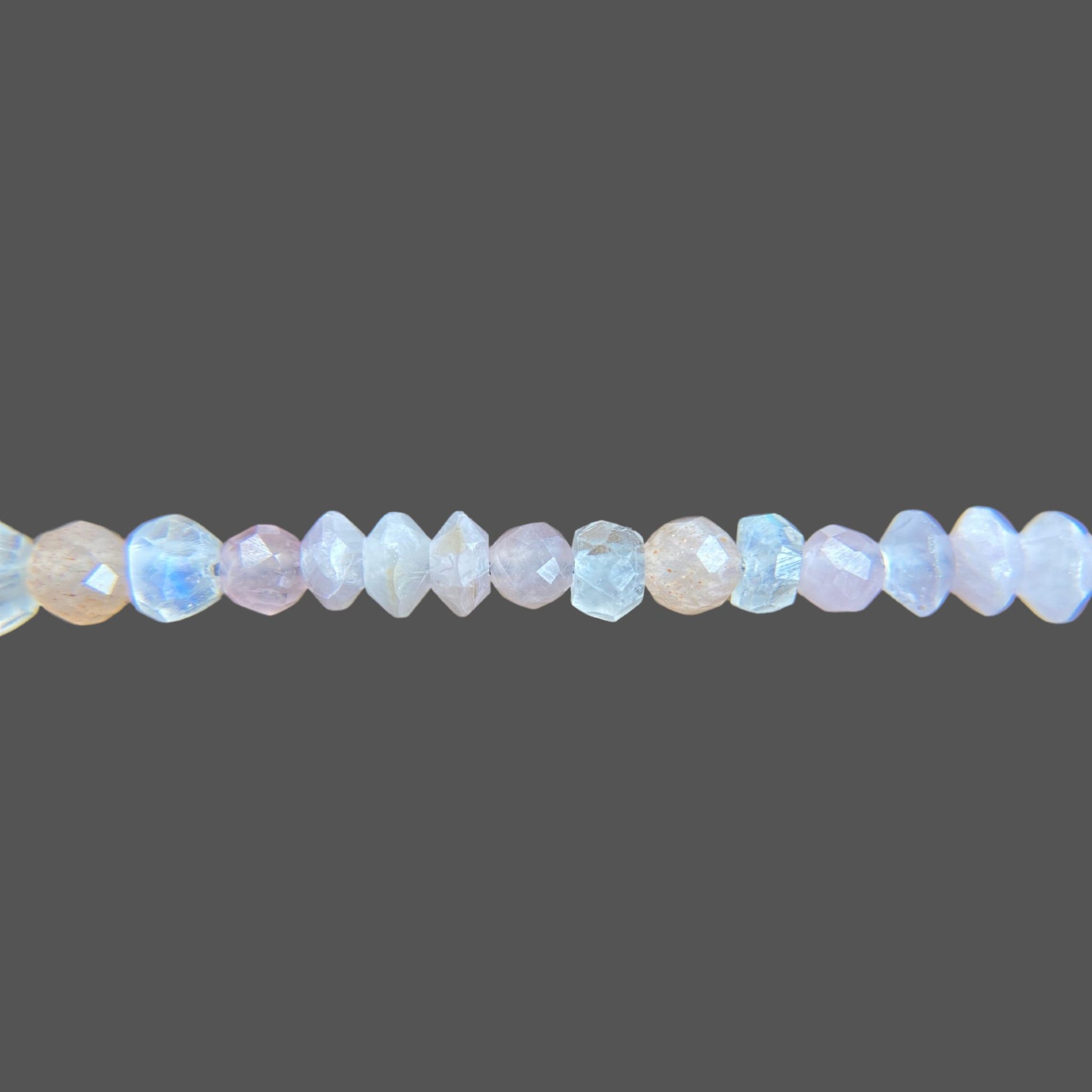 Close-up of gemstones on a beaded bracelet, featuring soft peach and pink hues of rose quartz, kunzite, and moonstone.