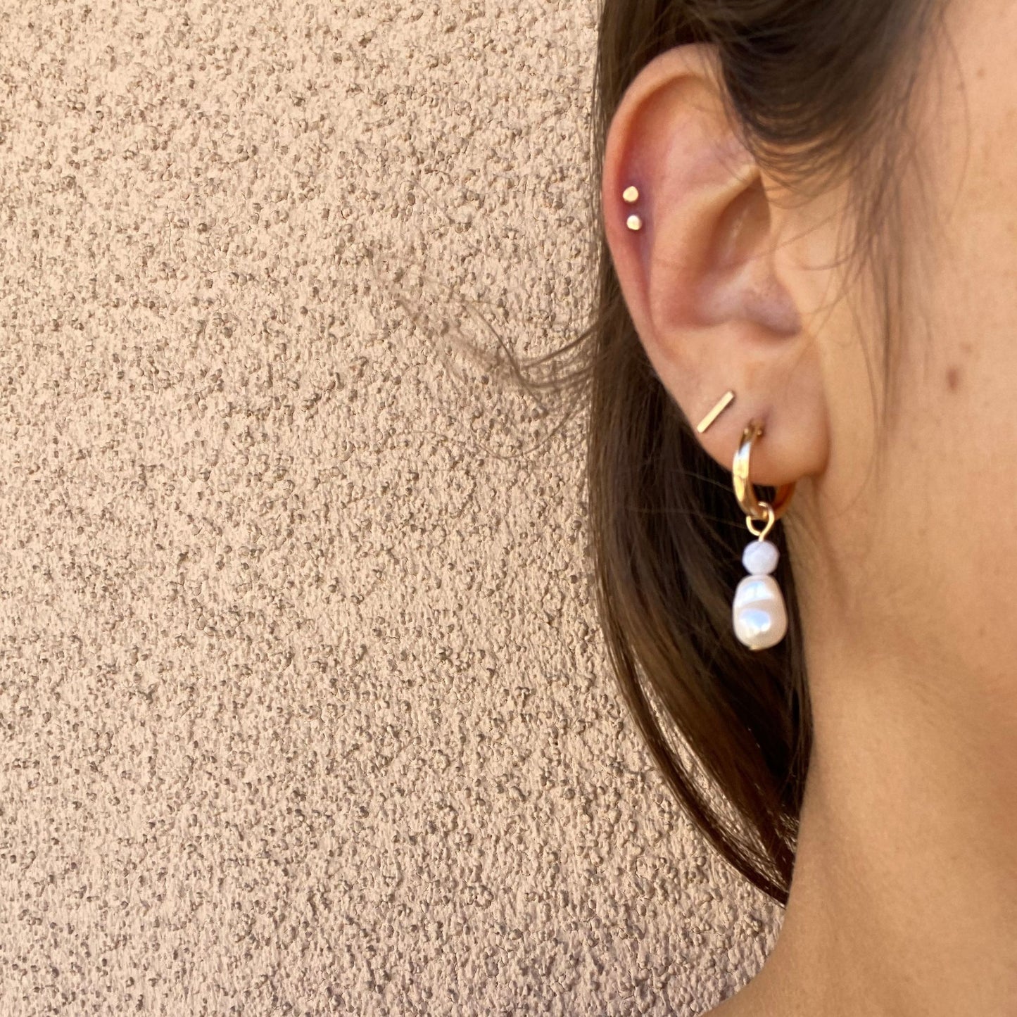 Gold hoop earrings with blue lace agate and freshwater pearl charms, shown on model. Only the model’s ear is visible.