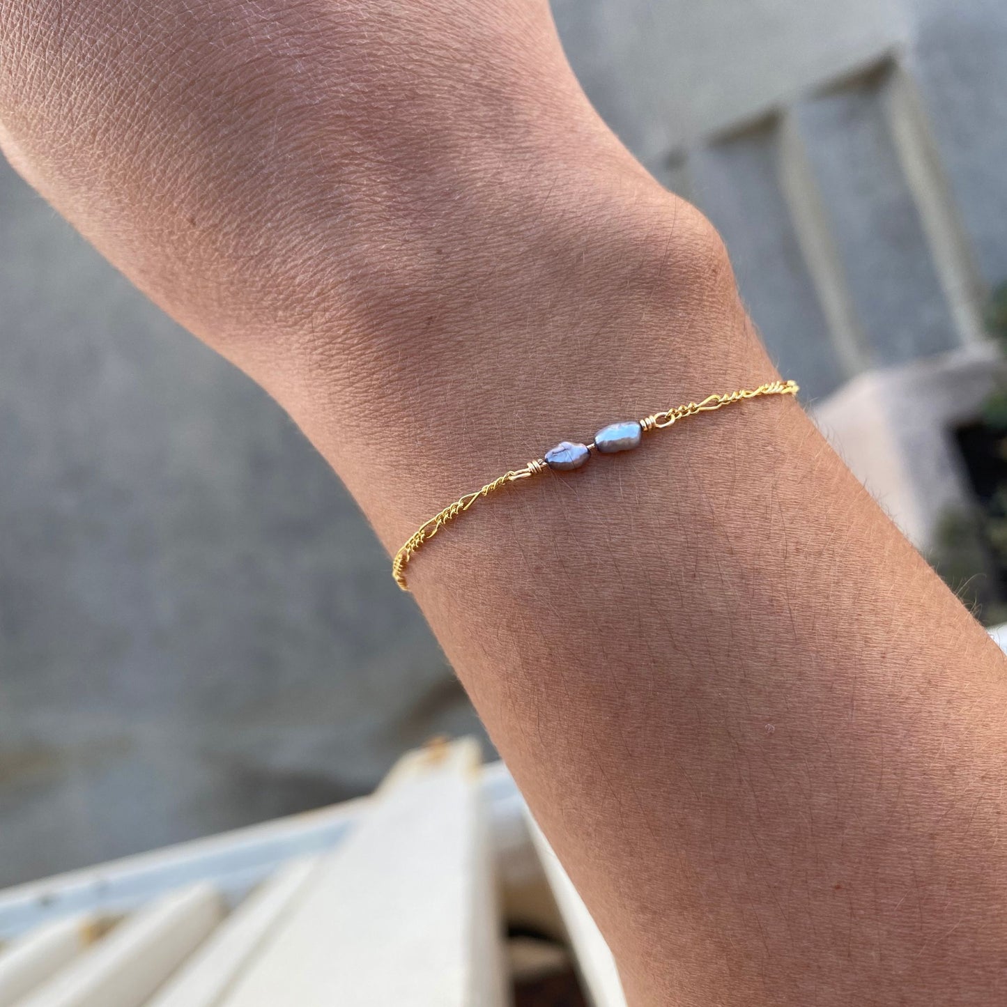 Minimal pearl bracelet with two irregular grey pearls centered on the chain, shown on model. Only model's wrist is visible.