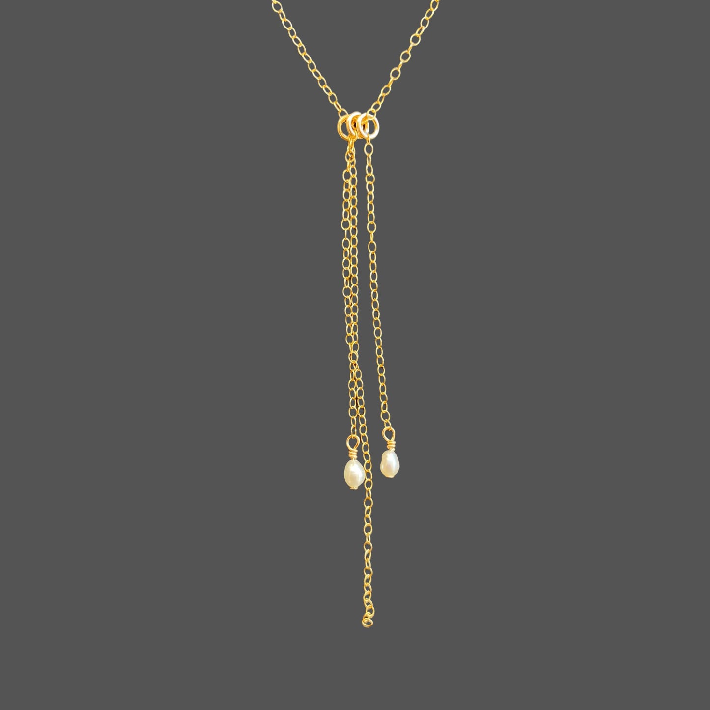 Close-up of the focal point on a pearl necklace with three hanging gold chains. Two chains ending in rice pearls, and one longer chain between them.