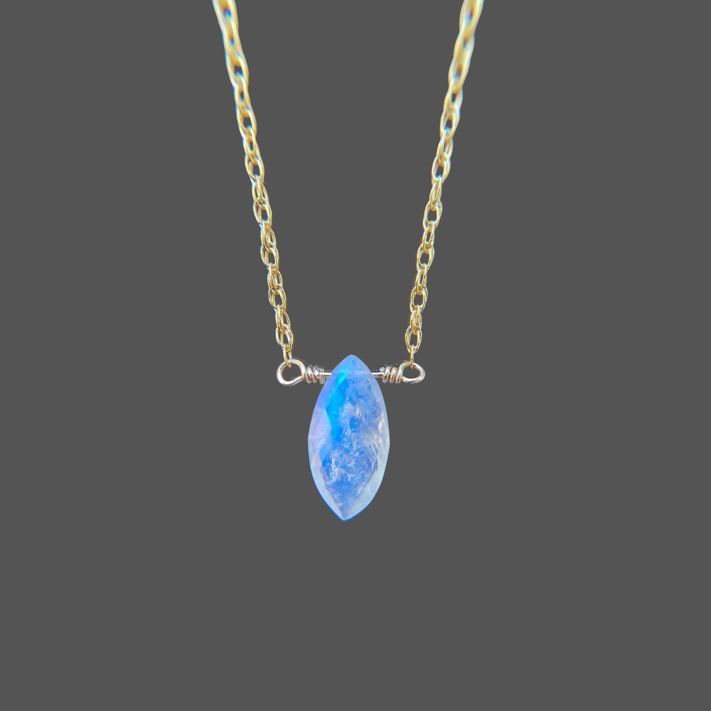 Close-up view of marquise shaped rainbow moonstone pendant on gemstone necklace with gold chain. Shown alone on plain background.