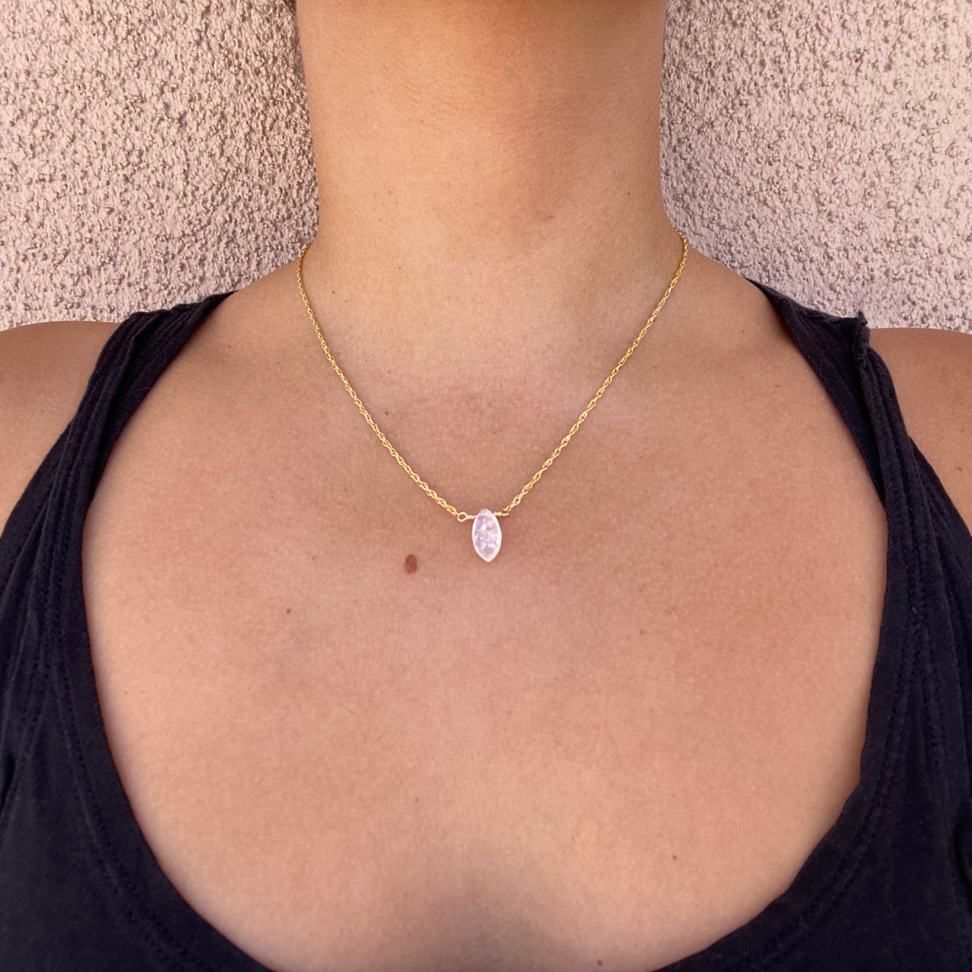 Pendant necklace with marquise shaped rainbow moonstone gemstone on a delicate gold rope chain. Shown on model, with only model’s neck visible.