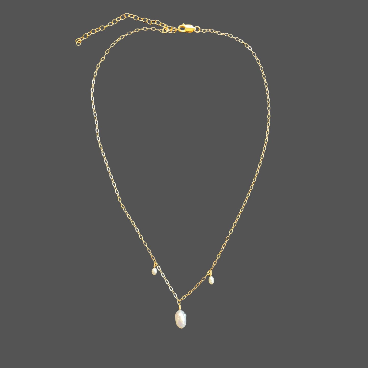 Pearl necklace on gold chain featuring three spaced pearls, a large pearl in the center with a rice pearl on each side. Shown on plain background.