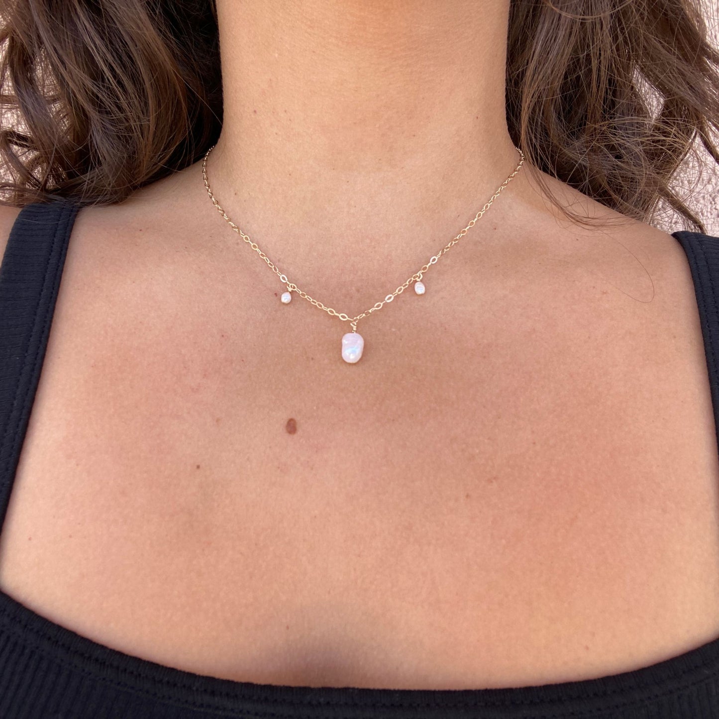 Pearl necklace on gold chain featuring a large pearl in the center with a rice pearl spaced on each side. Shown on model, with only the neck visible.