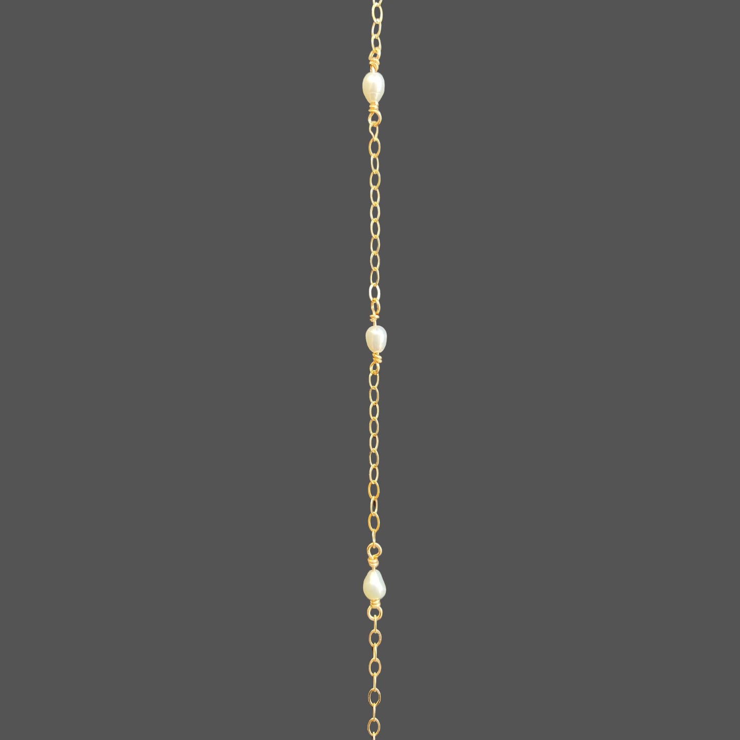 Close-up view of pearl bracelet, featuring three rice pearls equally spaced along the gold chain.