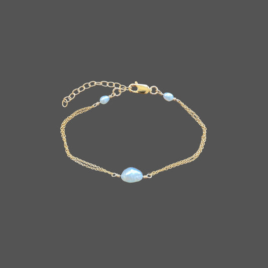 Dainty pearl bracelet with two strands of gold chain, featuring a freshwater pearl at the center and one small rice pearl at each closure.