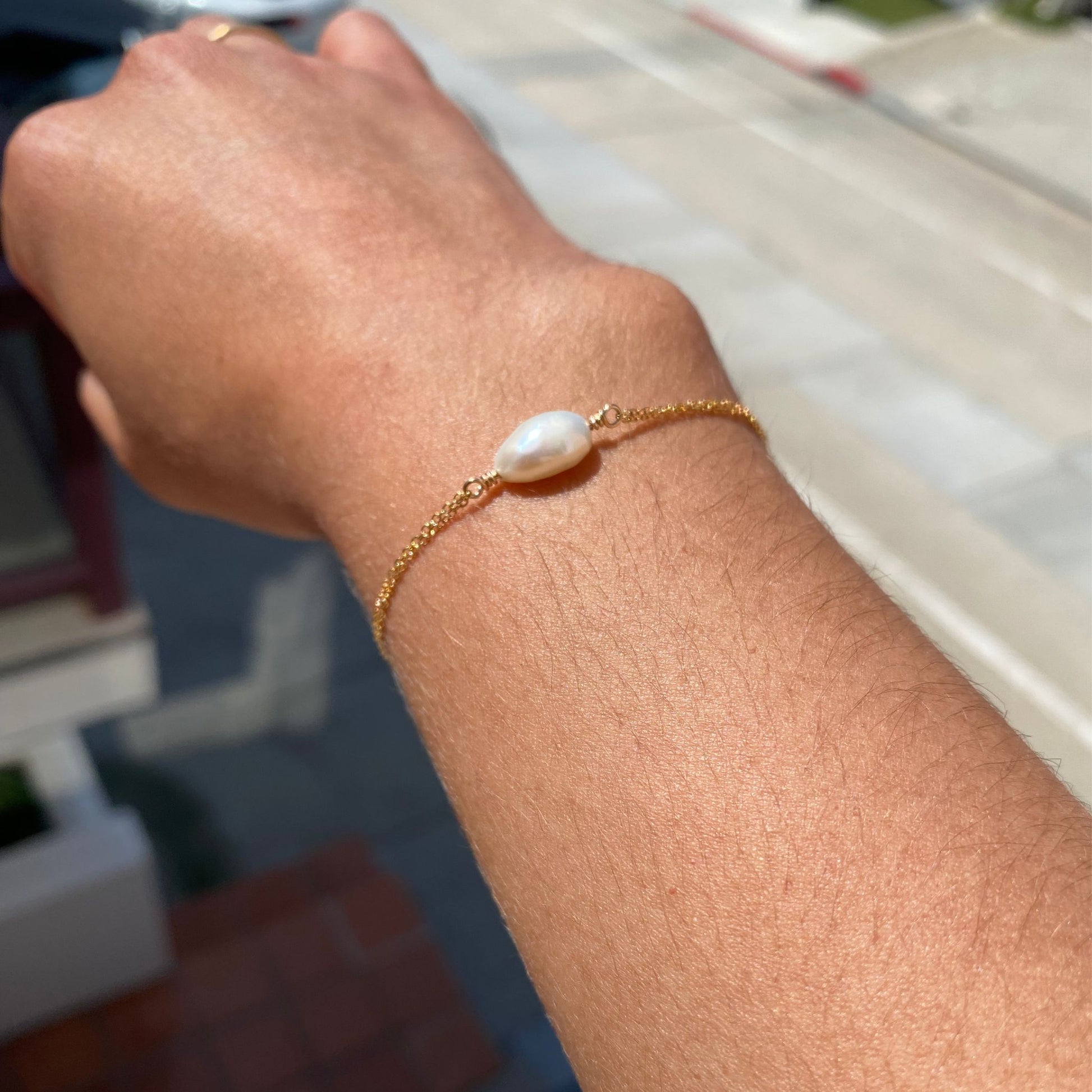 Pearl bracelet with pearl centered on two gold chains, shown on a model. Only the model's wrist is visible.