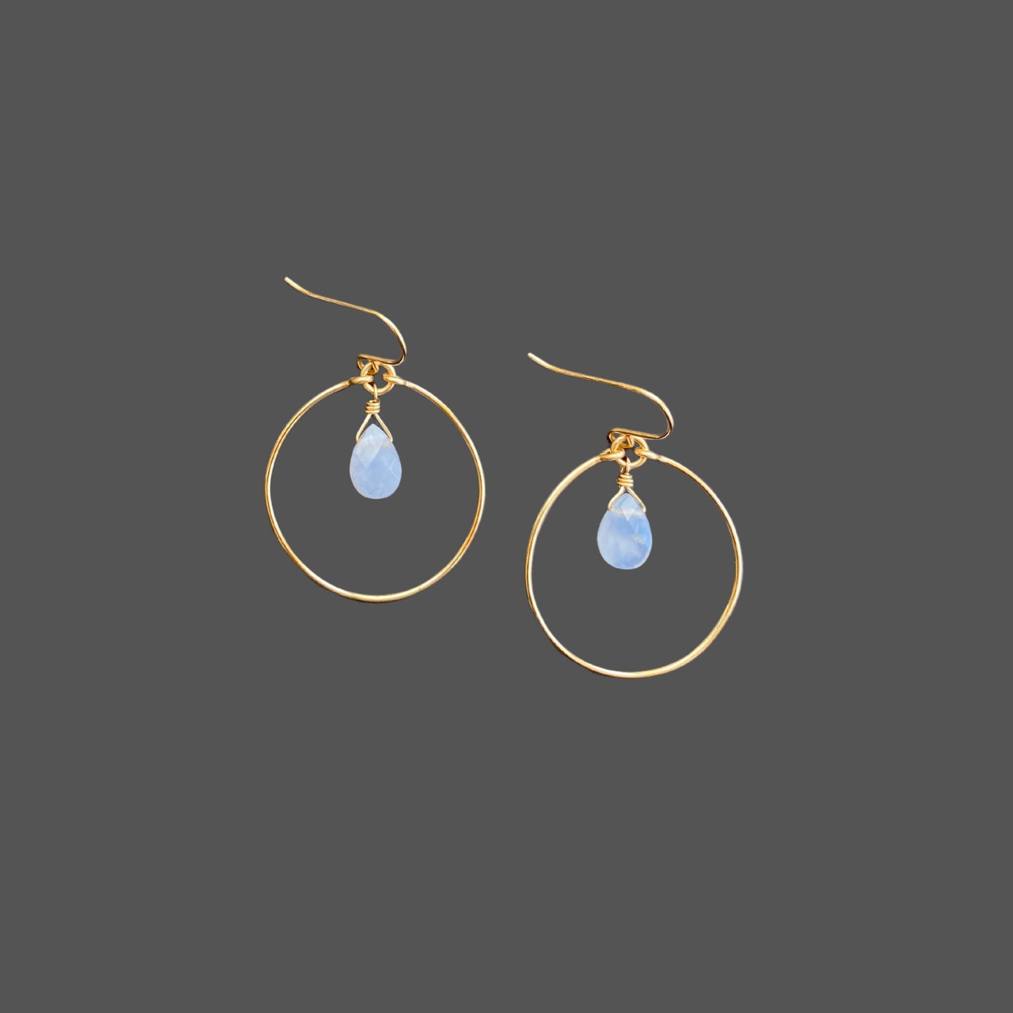 Gold hoop earrings with French earwires, featuring a blue chalcedony gemstone hanging from the top center of the hoop.