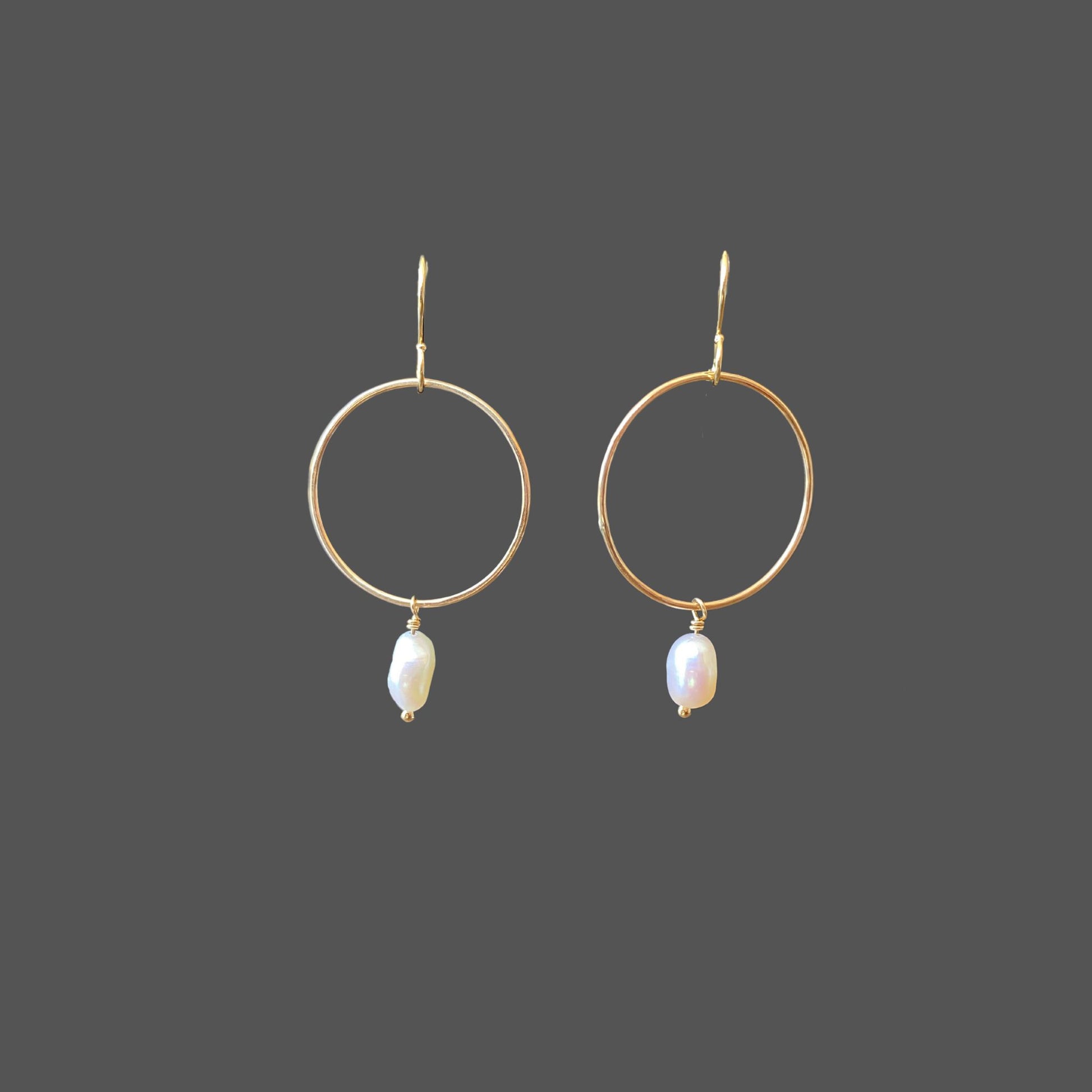 Front view of gold hoop earrings with a small freshwater pearl hanging from the bottom of the hoop.