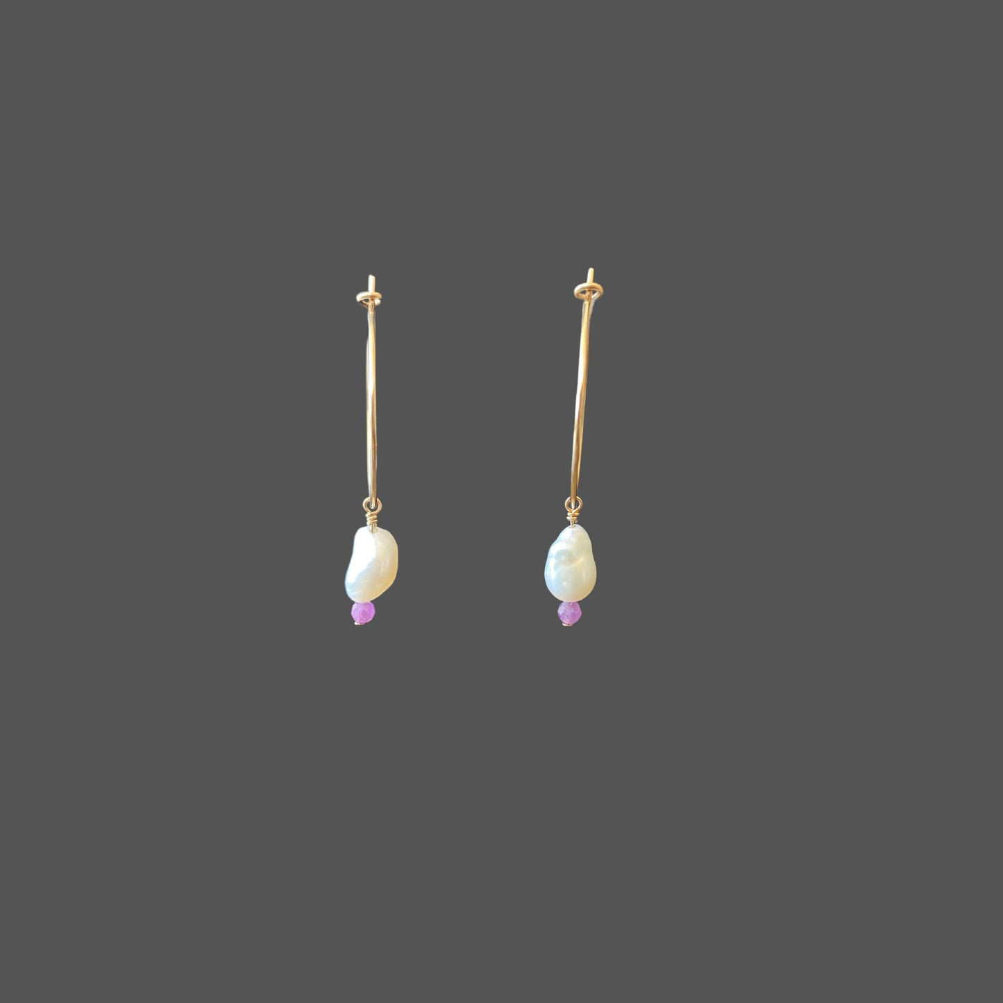 Front view of pearl earrings on a gold hoop with a freshwater pearl and a purple sapphire bead hanging from the bottom of the hoop.