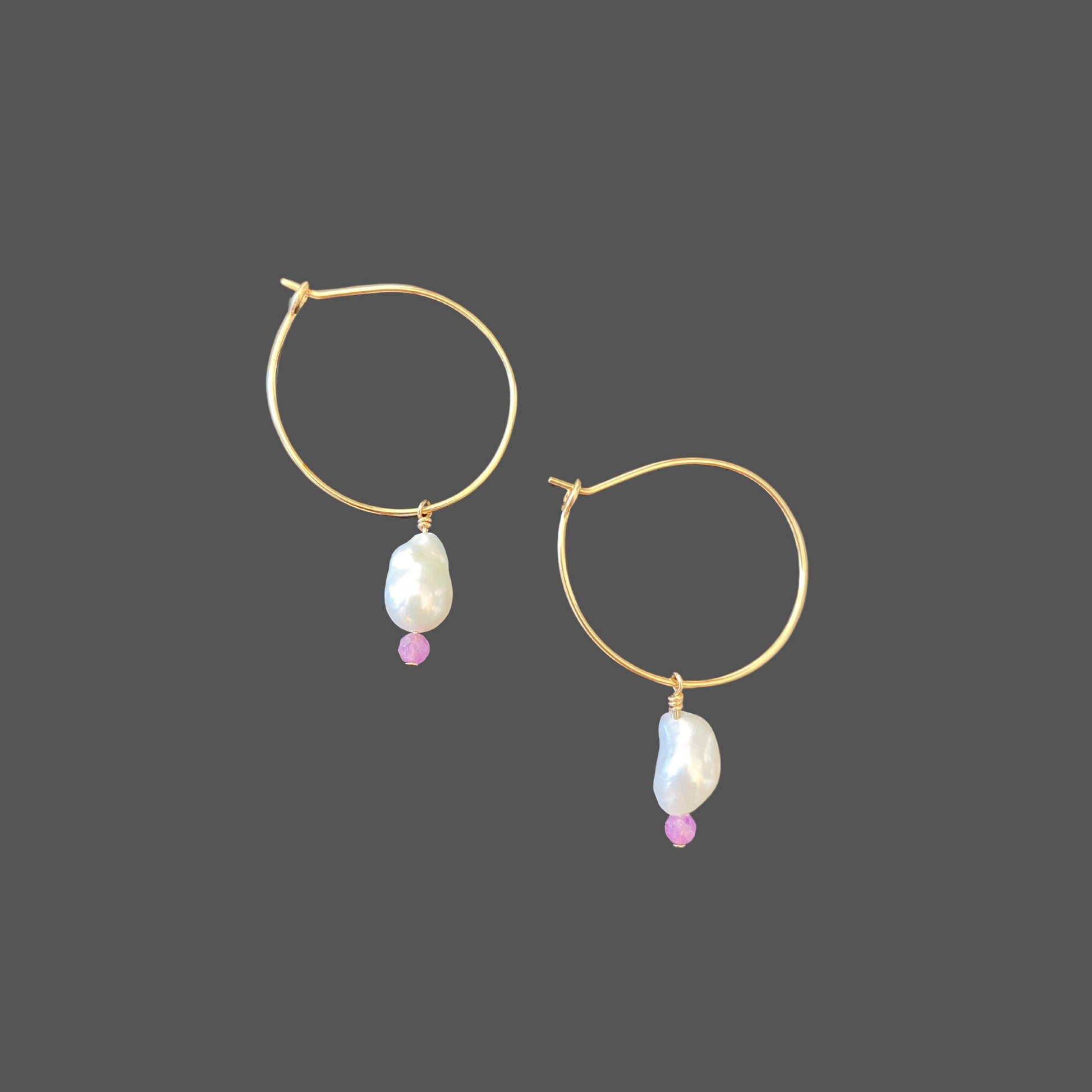 Side view of gold hoop earrings with a small freshwater pearl and a purple sapphire bead hanging from the bottom of the hoop.