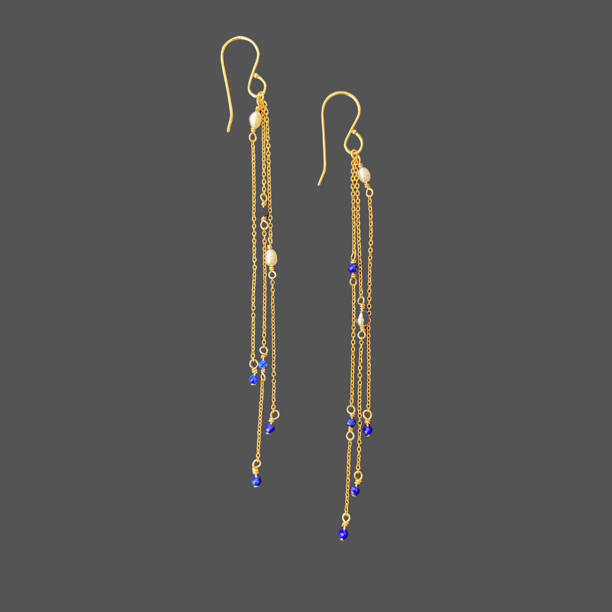 Side-view of long pearl earrings with three strands of gold chain, interspersed with pearls and lapis lazuli gems. Shown alone on plain background.