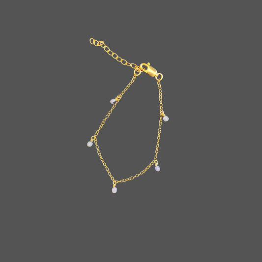 Dainty gold chain bracelet with five evenly spaced tanzanite beads dangling from the chain. The beads are a soft purple color.