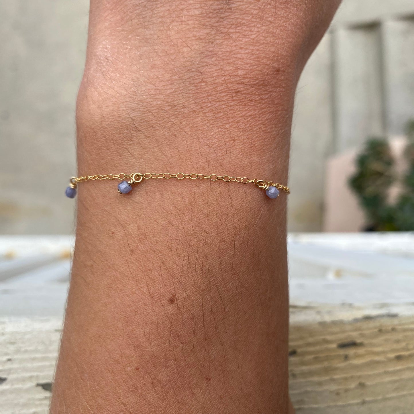 Gold chain bracelet with purple tanzanite gemstones hanging from the chain, shown on model. Only the model's wrist is visible.