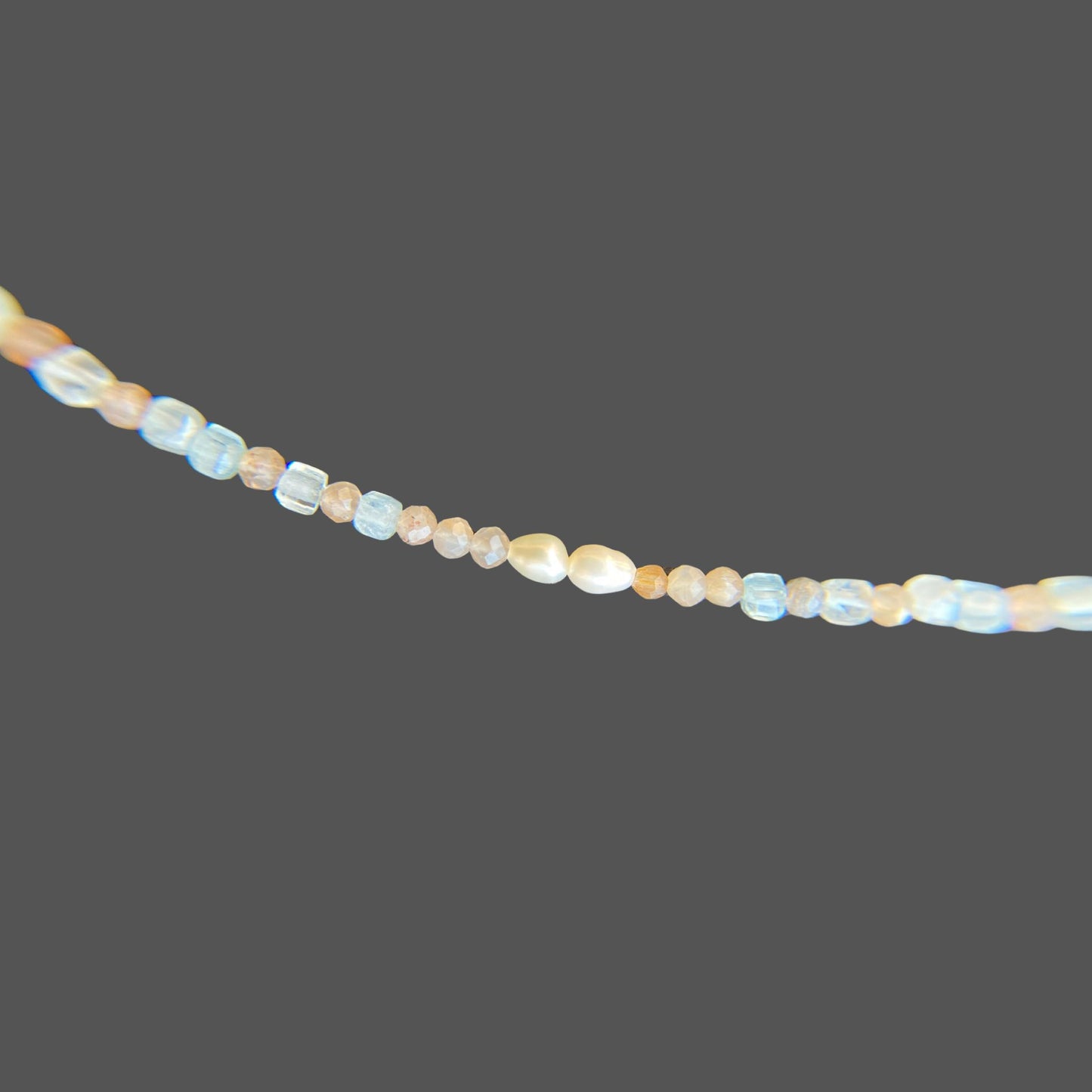 Close-up view of pearls and gemstones on beaded necklace, with aquamarine and sunstone gems in the colors of sunset. Shown alone on plain background.