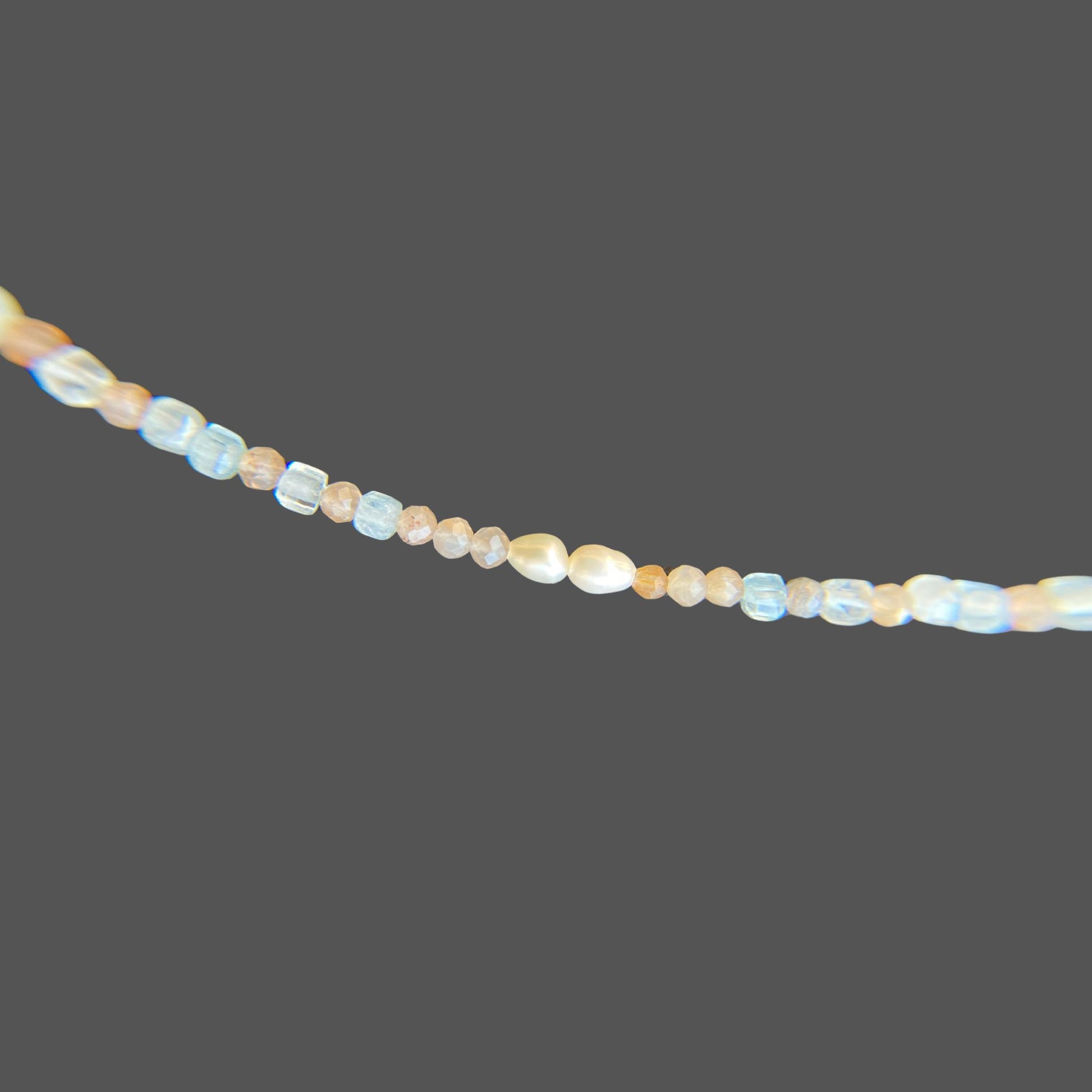 Close-up view of pearls and gemstones on beaded necklace, with aquamarine and sunstone gems in the colors of sunset. Shown alone on plain background.