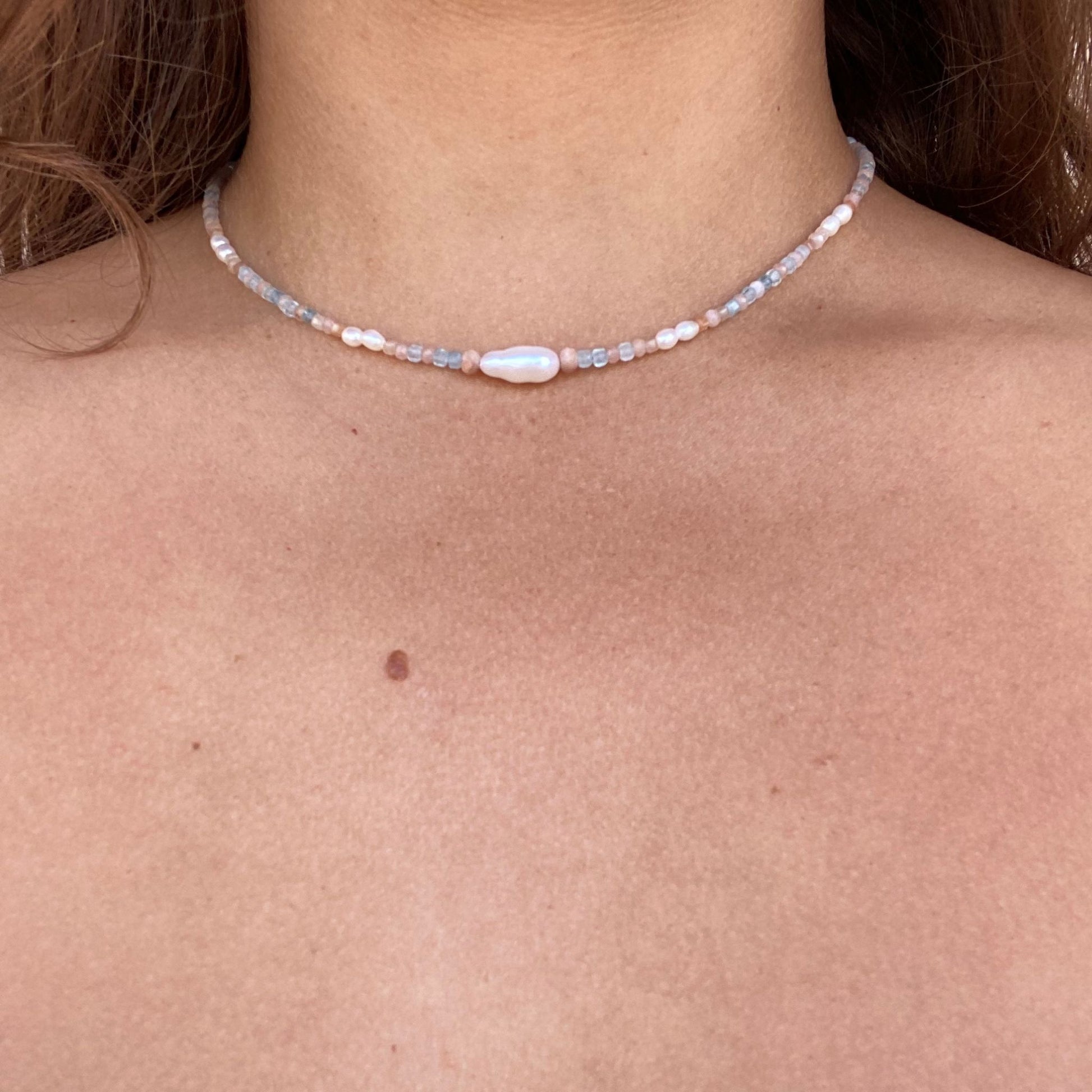 Pearl necklace shown on model, with pearls, soft pink sunstone, and baby blue aquamarine gemstones. Only model’s neck is visible.