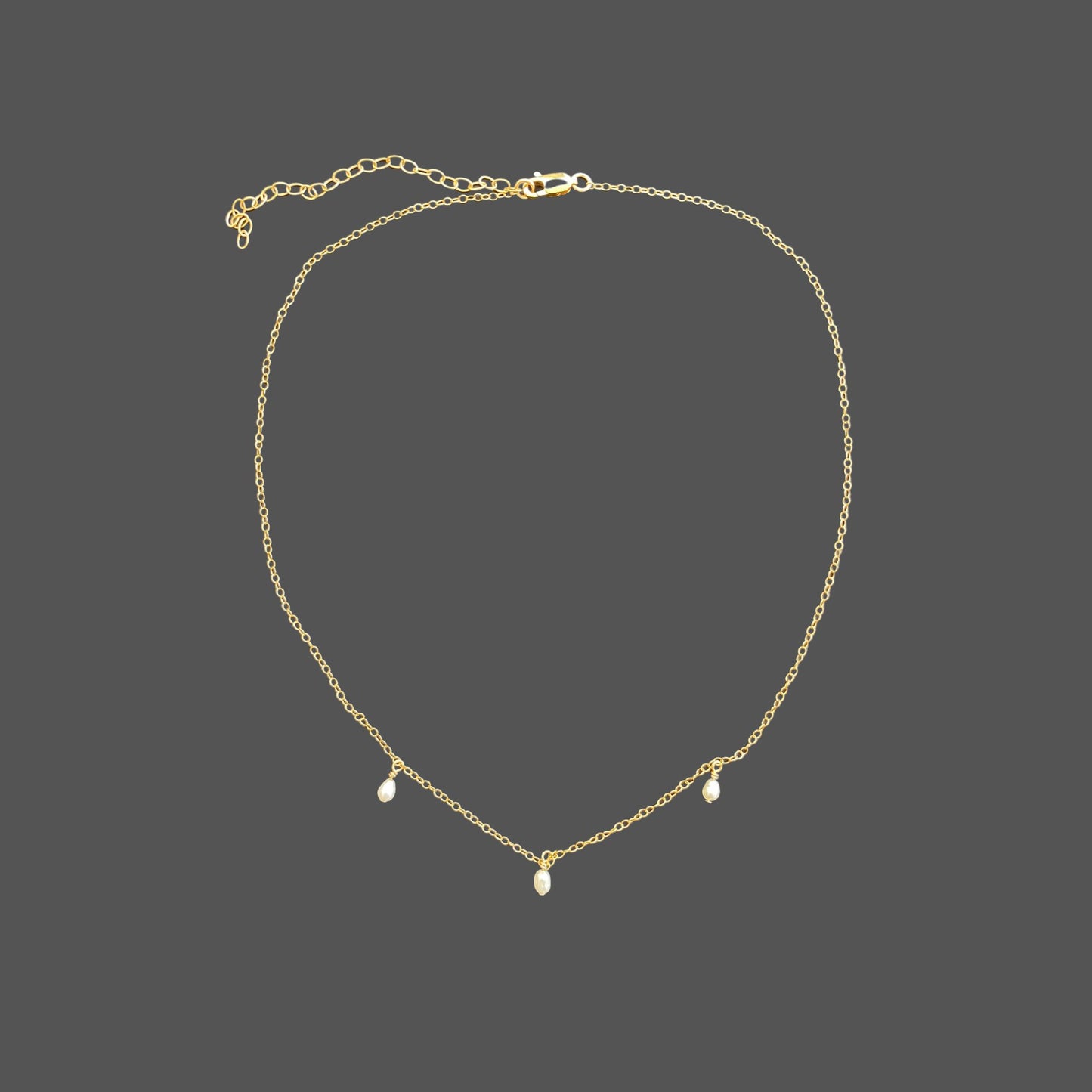 Pearl necklace with delicate gold chain and three equally spaced rice pearls dangling from the chain at its center. Shown alone on plain background.