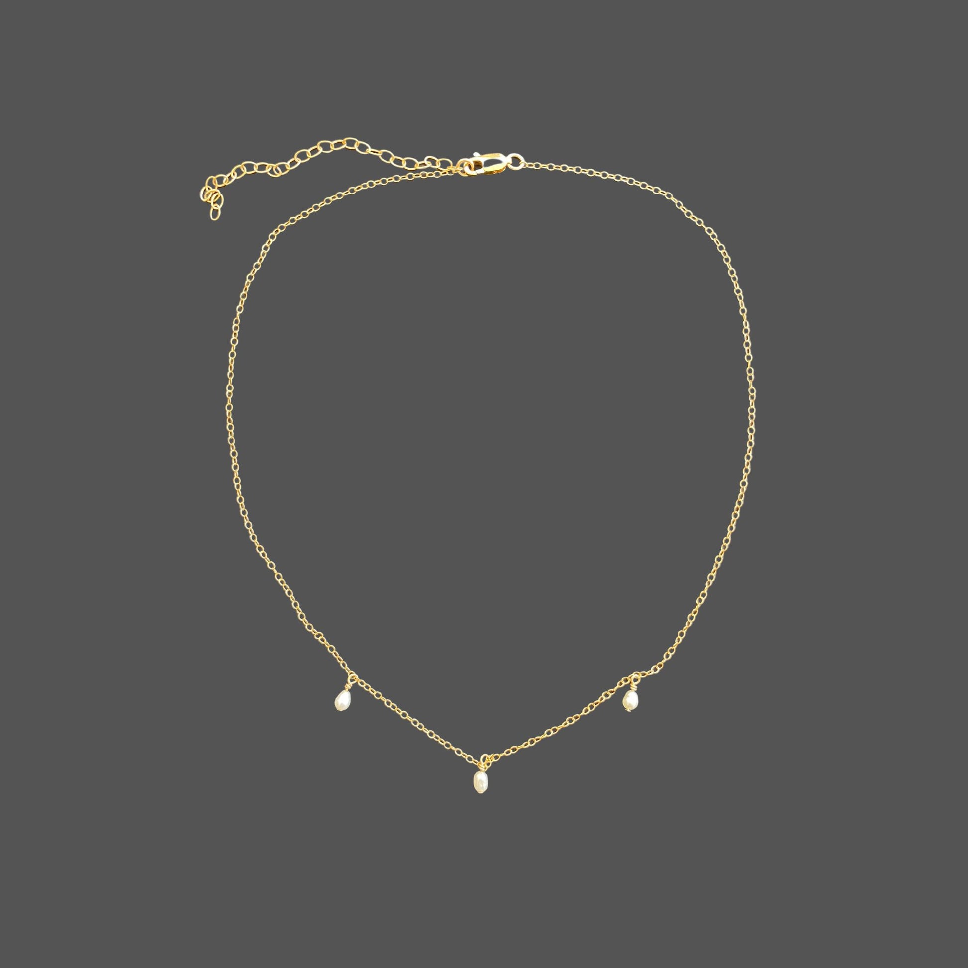 Pearl necklace with delicate gold chain and three equally spaced rice pearls dangling from the chain at its center. Shown alone on plain background.