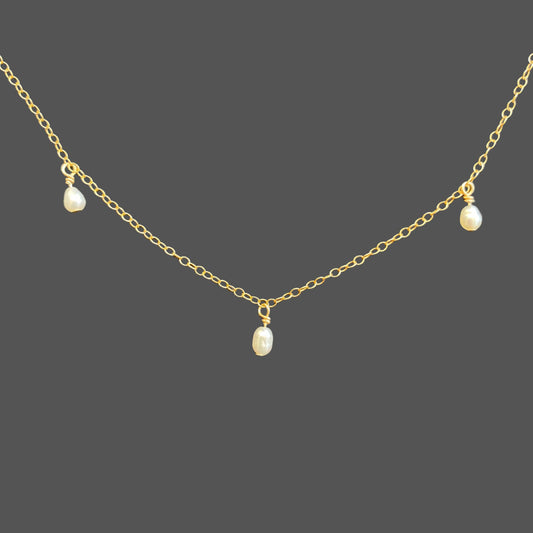 Close-up view of pearl necklace, showing three spaced rice pearls hanging from the center of a delicate gold chain. Shown alone on plain background.