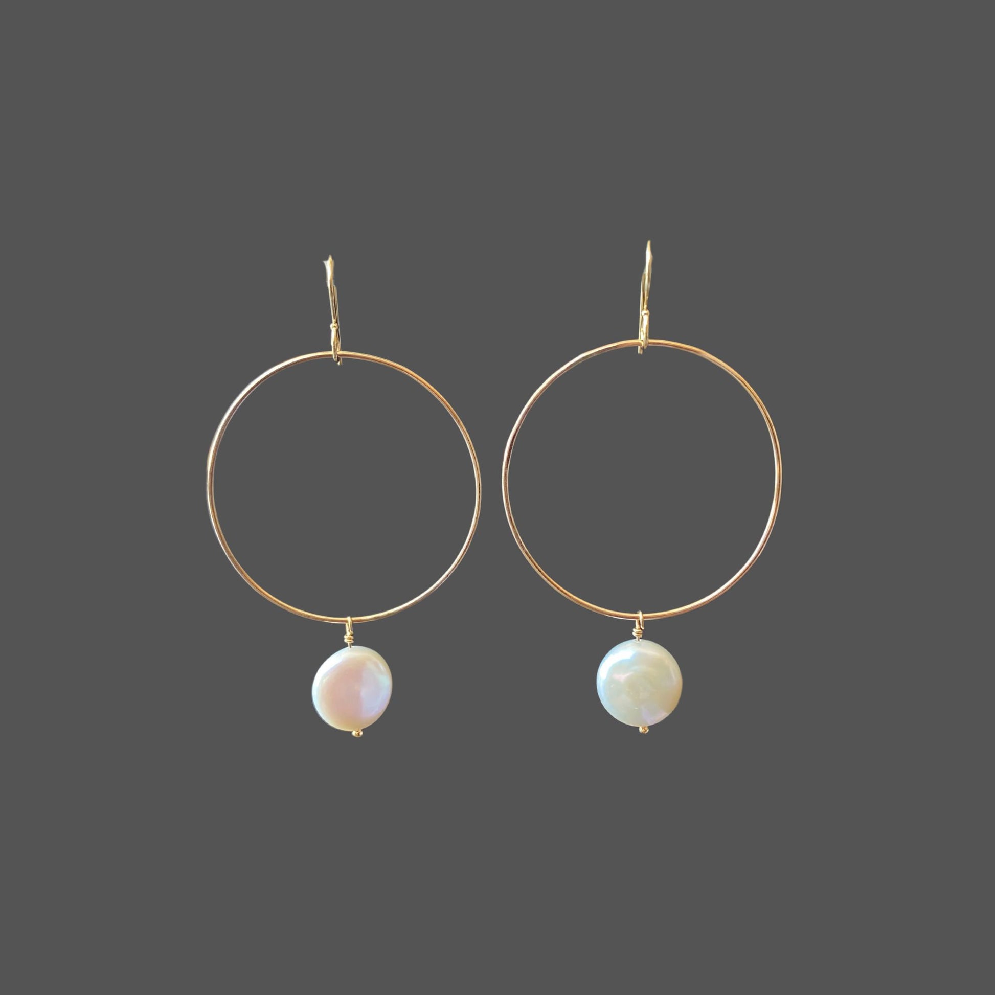 Front view of gold hoop earrings with a round freshwater coin pearl hanging from the bottom of the hoop.