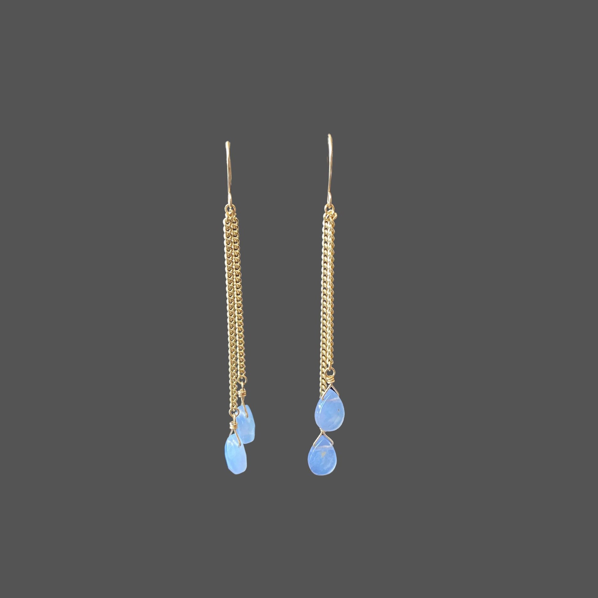 Front view of long earrings with asymmetrical gold chains ending in blue chalcedony gemstones. Shown alone on plain background.